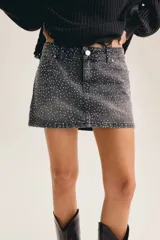 Minifalda de denim negro con aplicación de strass en toda la superficie, tiro medio y ruedo desmechado.