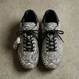 Championes tipo derby con capellada de cuero con textura de pelo y estampado animal print de cebra. Cuenta con suela de goma y cordones negros.