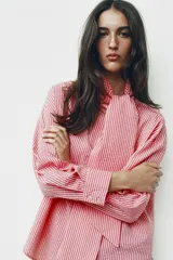 Camisa de rayas rosadas y blancas, con cuello subido decorado con un lazo integrado, manga larga con puños abotonados y cierre frontal oculto.