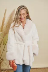 Abrigo de piel sintética color crudo, con cuello solapa, puños de piel más larga y cinturón del mismo material para ajustar a la cintura.