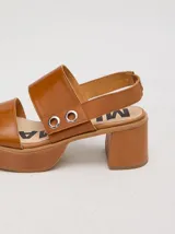 Sandalias de plataforma con taco cuadrado de 6 cm y base de 3 cm. Presentan dos tiras anchas en el empeine con detalles de doble argolla metálica en los laterales y una correa trasera con elástico para mayor ajuste.