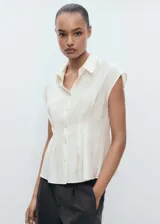 Camisa blanca sin mangas con pinzas en la cintura, cuello camisero y cierre frontal con botones.