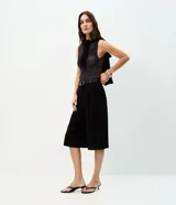 Bermuda de sastrería negra de tiro alto, confeccionada en crepé, con pinzas delanteras, perneras amplias, largo midi y cinturón incluido de poliuretano con hebilla metálica.