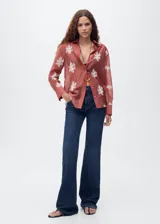 Camisa de manga larga en color terracota con diseño semitransparente. Presenta cuello camisero, cierre frontal con botones y bordados florales en color blanco distribuidos por toda la prenda.