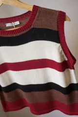 Chaleco tejido artesanal con hilado 70% algodón y 30% acrílico, a rayas horizontales en colores marrón, negro, blanco y rojo. Con cuello y sisas acanaladas en color rojo. Hecho en Uruguay.