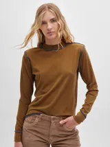 Polera de manga larga confeccionada en tela rib color marrón, con cuello alto y hombreras. Presenta detalles de costuras a la vista con hilo en color azul en el cuello, hombros, puños y ruedo.