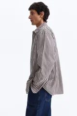 Camisa de algodón suave con cuello inglés, tapeta clásica y canesú en la espalda. Modelo de manga larga con puños abotonados y bajo levemente redondeado. Presenta diseño a rayas en tonos marrón y blanco.