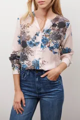 Camisa de manga larga con cuello redondo y cierre frontal de botones. Presenta un estampado floral en tonos azules y marrones sobre una base de color rosado claro.