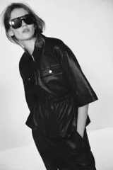 Chaqueta efecto piel color marrón, con cuello solapa, mangas por debajo del codo, cintura elástica, falsos bolsillos delanteros y cierre frontal con cremallera.