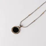 Collar con cadena de eslabones trenzados en plata con detalles en oro, que sostiene un dije circular con piedra ónix negra central y borde en oro.