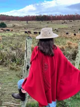 Capa roja de lana con apliques de cuero en los hombros y en el borde de la abertura frontal.