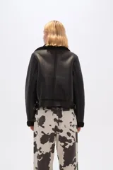 Campera corta negra de cuero sintético con cuello y puños de piel sintética negra, cierre frontal con cremallera y bolsillos laterales con cremallera.