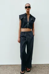 Chaleco de denim oscuro con cuello solapa, cierre frontal con cremallera metálica y bolsillos delanteros con tapeta. Presenta un diseño de corte abullonado con bajo elástico.