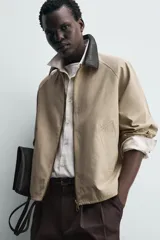 Sobrecamisa de corte relajado color beige, con cuello solapa en efecto piel de color negro. Presenta cierre frontal con cremallera, bolsillos de vivo en la cadera y mangas largas con puños ajustables.