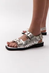 Sandalias plateadas de cuero con suela negra, punta cuadrada, dos correas anchas sobre el empeine con hebillas metálicas y detalle de ojales metálicos.