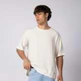 Remera oversize de lino entramado color blanco off-white, con cuello redondo, mangas cortas de hombro caído y etiqueta aplicada en el borde inferior.