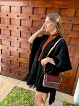 Ruana tejida en lana, de color negro, con diseño de flecos en los bordes inferiores.