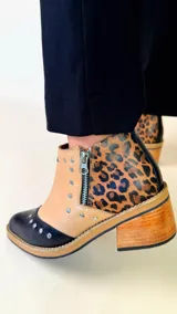 Botín de cuero bicolor con puntera negra, laterales en tono tostado y talón con estampado animal print. Cuenta con taco bloque de madera, cierre lateral y aplicación de tachas metálicas.