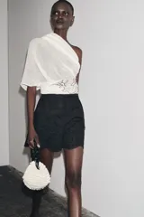 Bermuda negra de tiro alto confeccionada en hilatura de algodón con bordados perforados a tono, forro interior y cierre con cremallera oculta en costura.