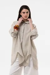 Camisa de lino color beige, de calce amplio y relajado, con cuello camisero, cierre frontal de botones, mangas largas y diseño de largo irregular con aberturas laterales.