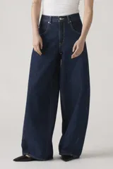 Jean de corte baggy y silueta barrel, confeccionado en denim rígido de color azul oscuro. Presenta costuras laterales curvadas que definen su forma característica, tiro alto y cierre frontal con botón y cremallera.