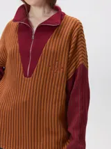 Pullover de tejido acanalado grueso con diseño bicolor en tonos marrón y bordó. Presenta cuello alto con cierre frontal, mangas largas y corte holgado.