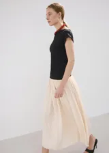 Vestido largo de diseño asimétrico con cuerpo negro entallado de cuello barco y manga corta, combinado con una falda larga evasé en color beige claro.