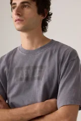 Remera de algodón con calce relajado, cuello redondo y mangas cortas. Presenta un efecto de lavado desgastado en color gris y el logo de la marca estampado en el pecho en un tono sutil.