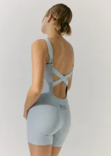 Monoprenda corta de tejido seamless, color celeste, con diseño de espalda descubierta con tiras cruzadas y logo estampado en la parte posterior.