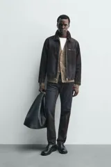 Cazadora de hombre de corte relajado, confeccionada en tejido con algodón de acabado flocado efecto terciopelo lavado, color marrón oscuro con efecto desgastado. Presenta cuello solapa, cierre frontal de cremallera, bolsillo con cremallera en el pecho y bolsillos laterales en la costura de la cadera.