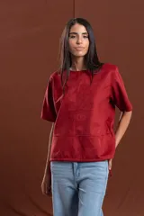 Remera de gamuza color rojo oscuro, con cuello redondo, mangas cortas y detalle de cortes verticales y horizontales que definen la silueta. Presenta cordones ajustables en el ruedo inferior.