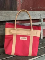 Bolso de playa grande con estampado camuflado en tonos verdes, asas de mano y detalles de tiras en cuero color tostado con hebilla decorativa. Cuenta con un parche de cuero con el logo de la marca en el frente.