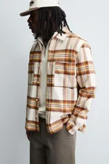 Camisa de corte relajado confeccionada en tejido con acabado de franela. Presenta diseño de cuadros en tonos beige, marrón y amarillo, cuello solapa, manga larga con puños abotonados, bolsillos plastrón en el pecho y cierre frontal de botones.