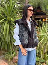 Chaleco reversible con un lado de piel sintética gris y el otro lado de tela bordada con diseño floral y espiral en tonos blanco y negro. Presenta un diseño sin mangas y corte recto.