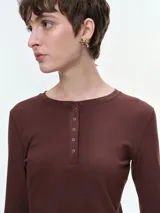 Remera de manga larga confeccionada en tejido acanalado, con escote redondo y cierre frontal con botones. Presenta un ajuste entallado al cuerpo.