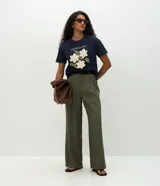 Remera de algodón color blanco, con cuello redondo y manga corta. Presenta un estampado con la frase 'Soy flor. Soy latina' y flores bordadas en relieve con textura tejida.