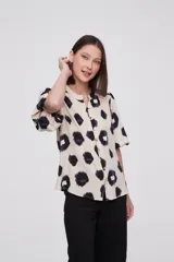 Blusa de manga corta con estampado de manchas negras y azules sobre fondo crema, cuello mao y cierre frontal con botones.