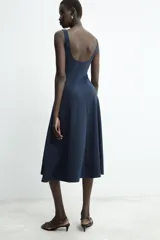Vestido midi de color beige con escote cuadrado y tirantes anchos. Presenta un diseño entallado en el torso con costuras verticales marcadas y falda con caída evasé.