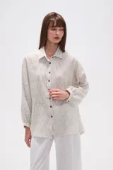 Camisa de corte holgado con cuello clásico y cierre frontal de botones. Presenta mangas largas con puños y un diseño de rayas verticales finas en tonos neutros.