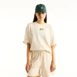 Remera oversize de color beige con cuello redondo y mangas cortas. Cuenta con un pequeño parche estampado en el centro del pecho con el logo de la marca en estilo colorido.