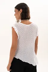 Blusa de textura rugosa en color blanco, sin mangas, con detalle de volados en los hombros y corte asimétrico en el ruedo.