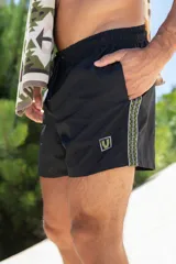 Short de baño negro con cintura elástica ajustable con cordón, bolsillos laterales y bolsillo trasero con cierre. Presenta una banda lateral con diseño geométrico en blanco, verde y amarillo.