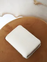 Billetera Actitud Sur de cuero con pelo vacuno en color blanco, con cierre perimetral y compartimentos internos de cuero.