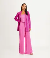 Pantalón pantalona color rosado, de textura satinada, con barras amplias, cierre de botón y cremallera, y pinzas.