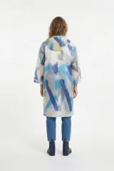 Piloto impermeable de corte recto y largo midi, con capucha ajustable mediante cordones. Presenta un diseño estampado con motivos botánicos en tonos verdes y amarillos sobre una base translúcida. Cuenta con cierre frontal mediante botones a presión y mangas largas.