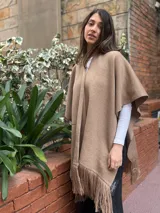 Ruana de tejido de lana merino color tostado, con diseño abierto, mangas cortas y detalle de flecos en el ruedo.
