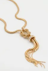 Collar largo dorado de cadena tipo serpiente con nudo decorativo central y detalle de anillo con incrustaciones de cristales, finalizando en tiras colgantes.