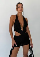 Vestido corto negro con textura arrugada, escote halter profundo y recortes laterales. Presenta un detalle de hebilla metálica dorada en el centro del busto que une las dos partes del corpiño.
