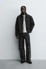 Cazadora de algodón color negro lavado, de corte relajado (relaxed fit), con cuello solapa a contraste, cierre frontal de cremallera, bolsillos canguro en la cadera y puños con botón a presión.