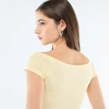 Camiseta de manga corta amarilla de punto calado, con escote bote y un pequeño lazo decorativo en el centro del pecho.
